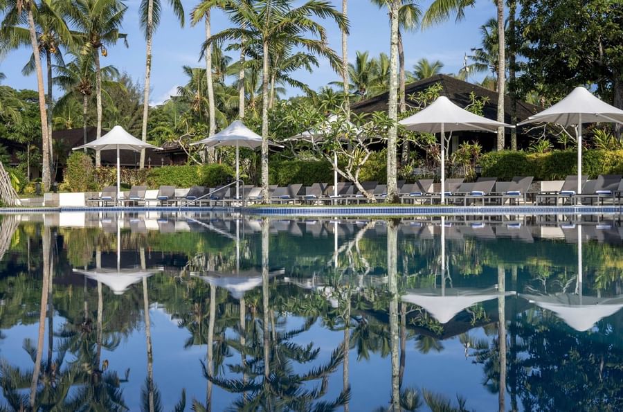 Serene pool with lounge chairs and umbrellas surrounded by lush palm trees at Warwick Le Lagon Vanuatu