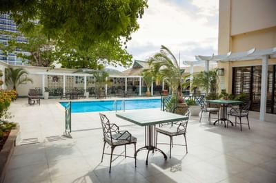 Dining tables arranged by the outdoor pool in Garden Terrace at Courtleigh Hotel & Suites