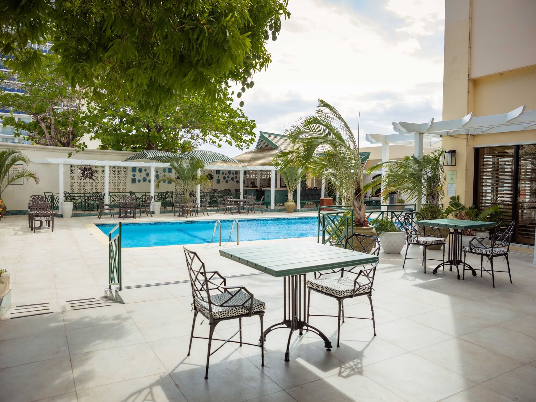 Dining tables arranged by the outdoor pool in Garden Terrace at Courtleigh Hotel & Suites