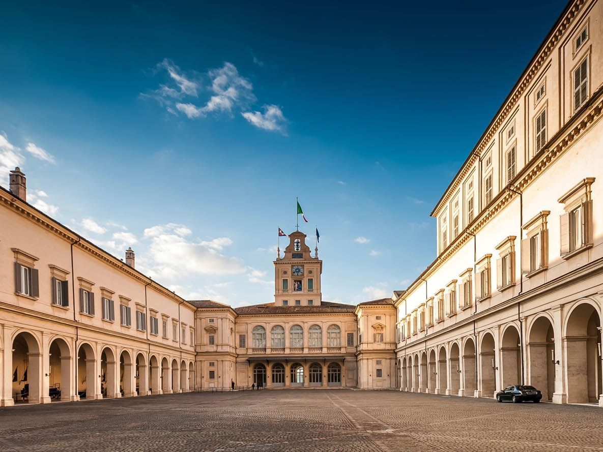 Quirinal Palace with clock tower and flags, surrounded by arches in a spacious courtyard near The Glam Hotel