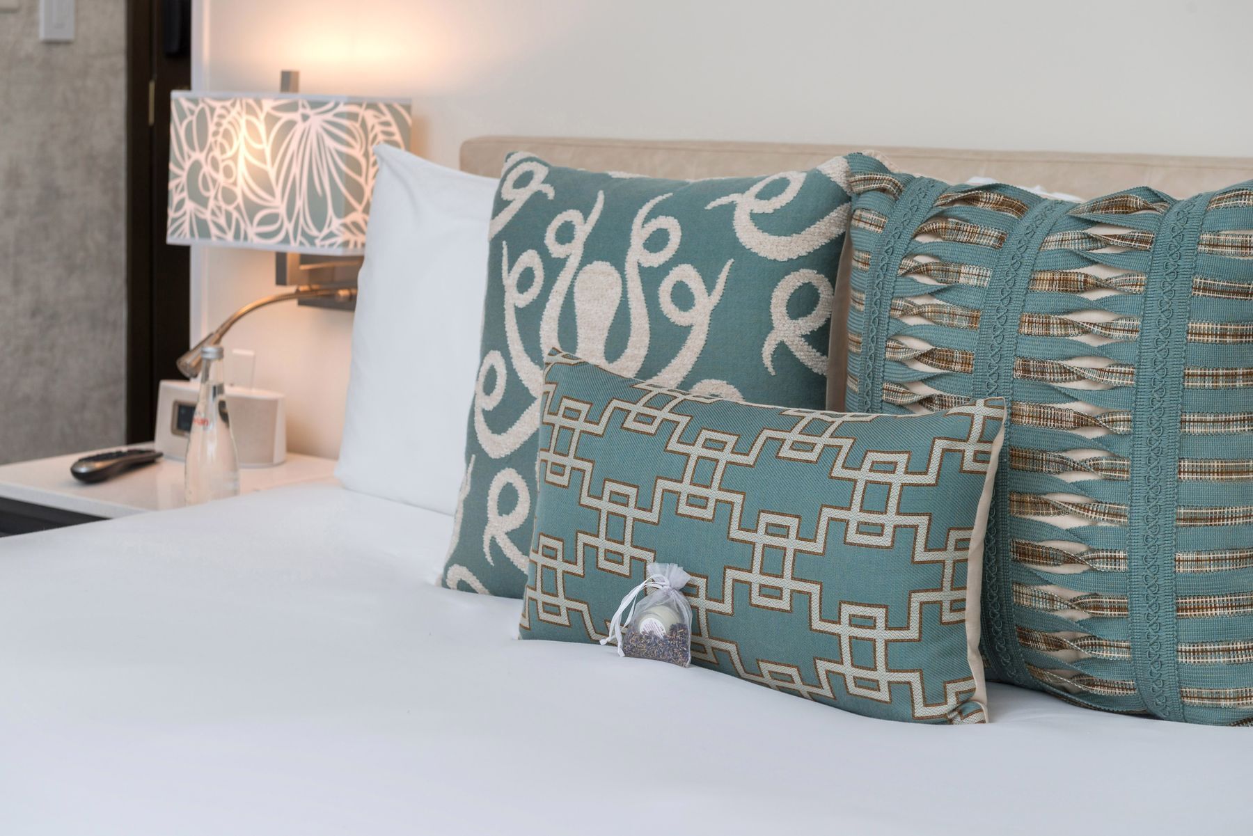 A close-up of a bed with decorative pillows and a lamp on a nightstand.