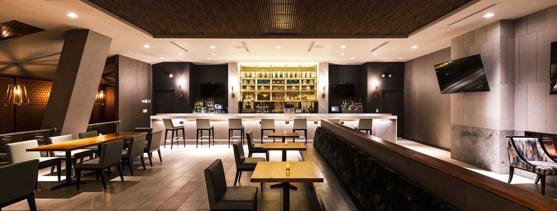 Bar counter with stools, a well-lit display of bottles, and tables in Bogart's Lounge at APA Hotel Woodbridge