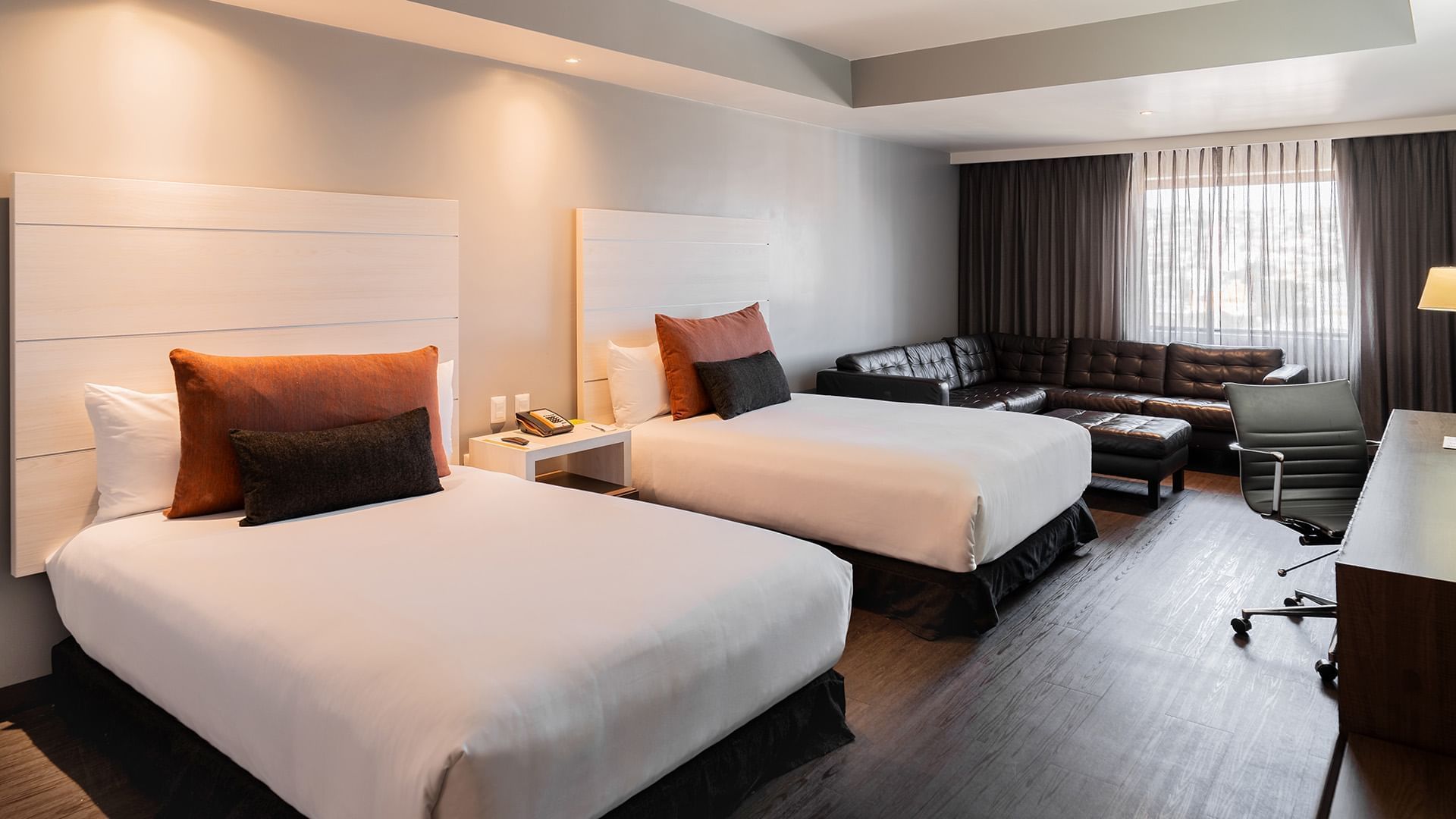 Nightstands & a black leather sectional sofa by the bed in the Two Double Junior Suite at Real Inn Tijuana