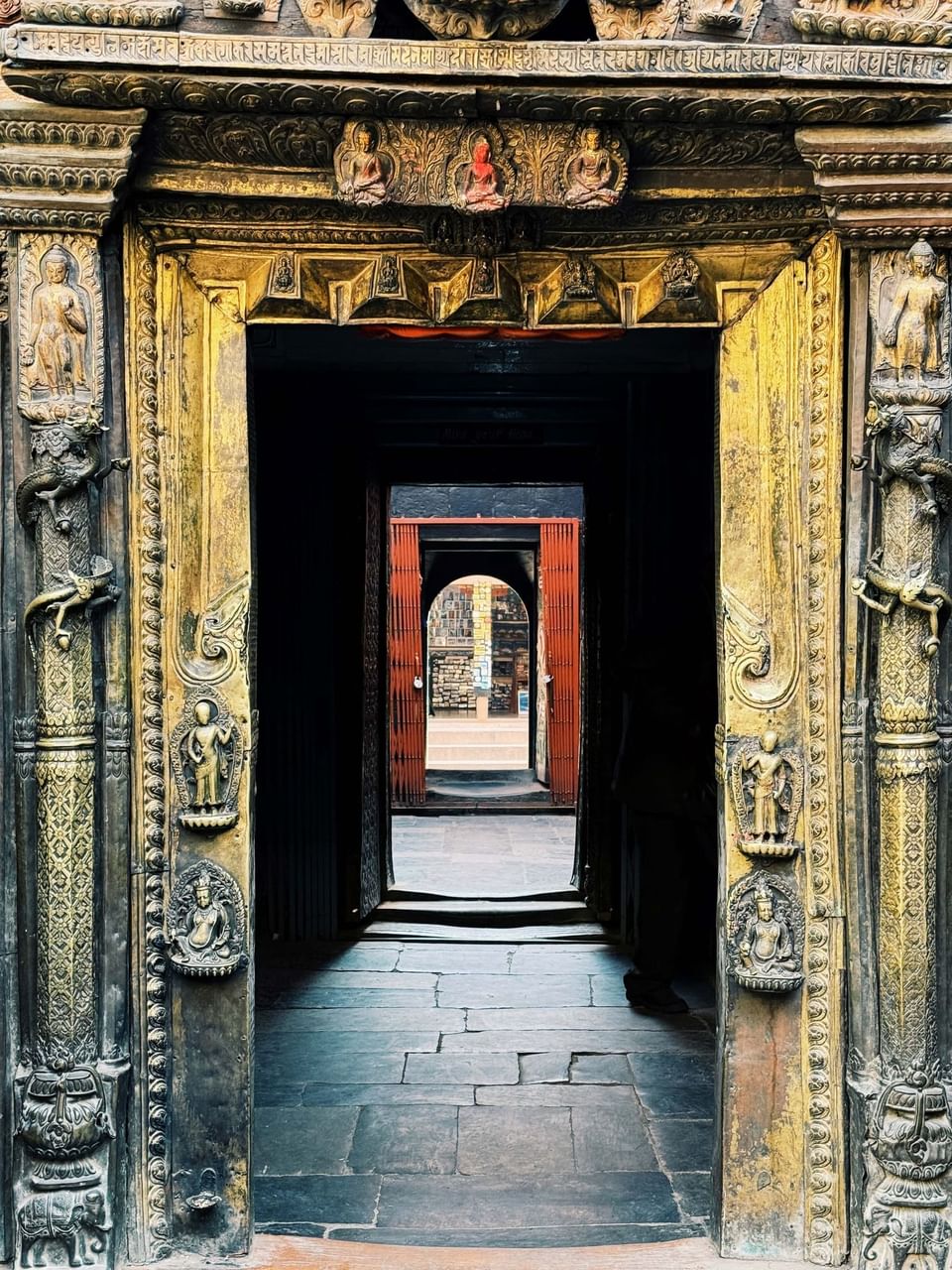 Carved golden doorway framing a view of an inner corridor, showcasing detailed sculpture at Dwarika's Hotel Kathmandu