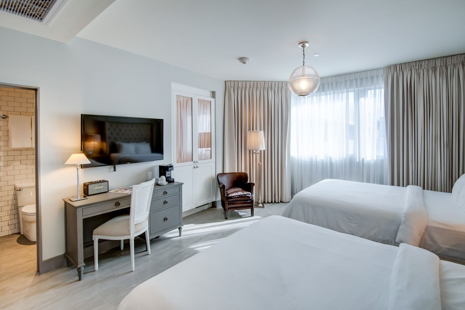 A hotel room with two double beds, a desk with a TV, and a window with curtains.