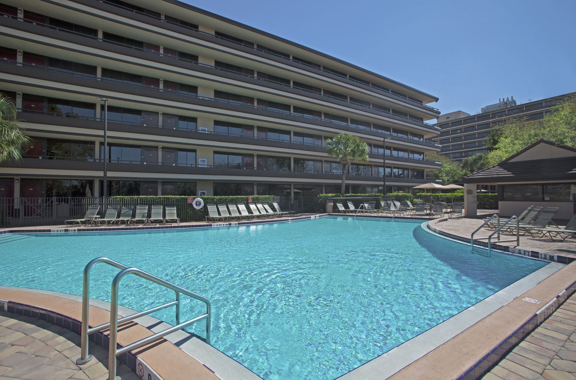 A large swimming pool with lounge chairs and a multi-story building in the background.