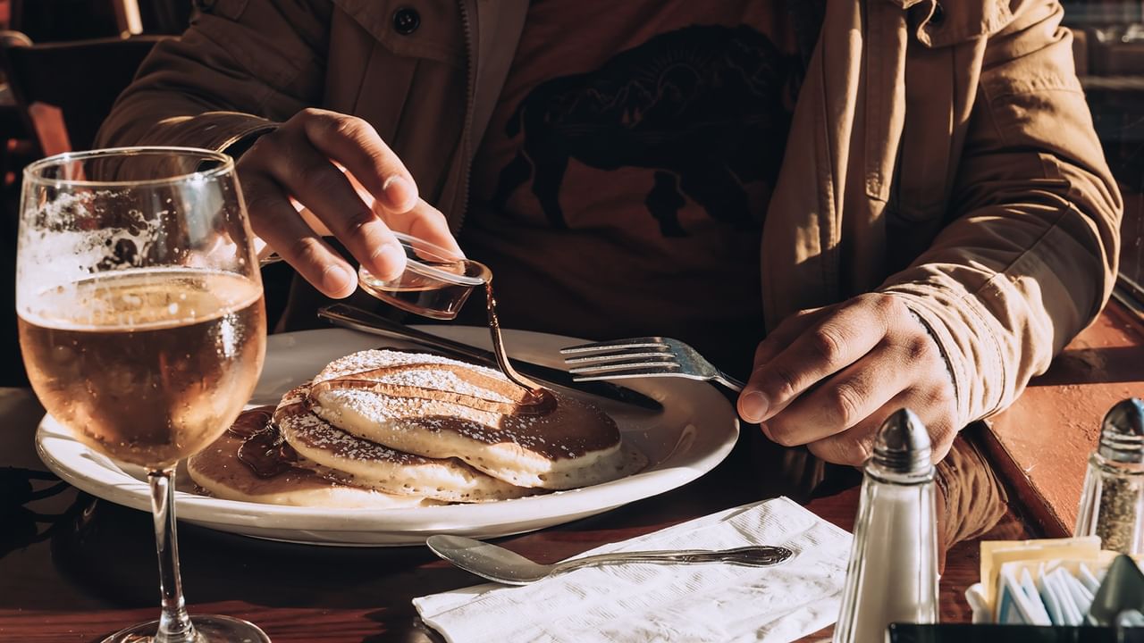 man pouring maple syrup on pancakes