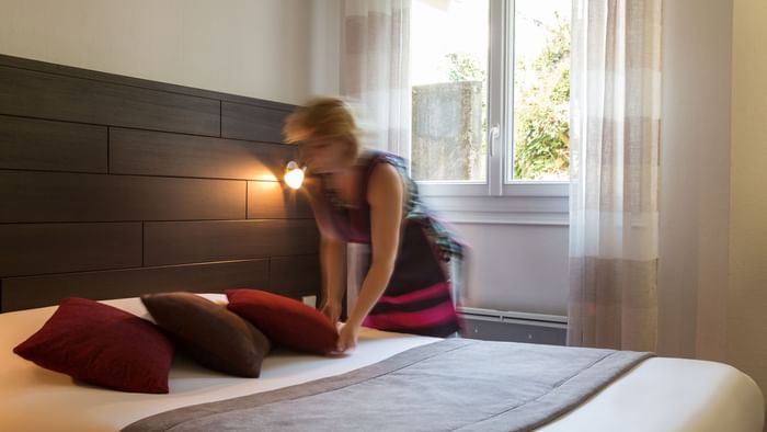 A maid preparing a bed in a room at Hotel du Chateau