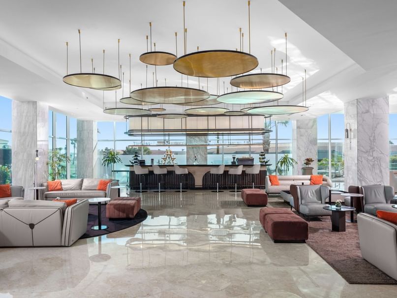 Lounge area with couches, bar, and large circular ceiling lights in a modern building with glass walls.