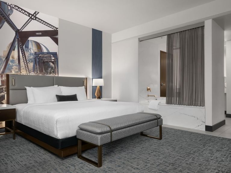 Longitude Suite with a bed and a large mural of a historic bridge on the wall, showing an open bathroom at Hotel 43 Boise