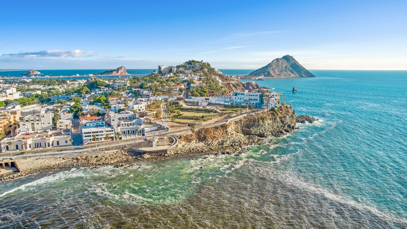 Aerial view of a vibrant coastal city and its rocky shoreline, with distant islands near Curamoria Collection