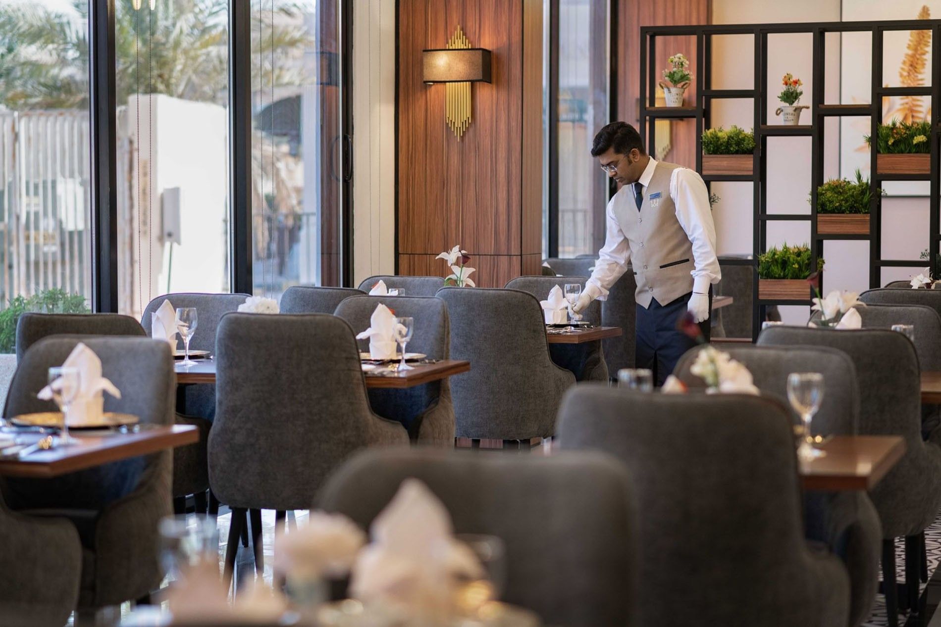 Waiter setting a table with glassware and napkins by a black metal room divider at Warwick Al Jubail