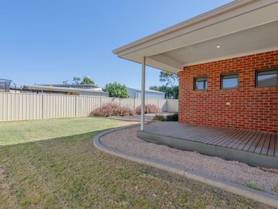 Backyard with wooden deck, brick house, and green lawn at La Trobe University Regional Housing – Mildura.
