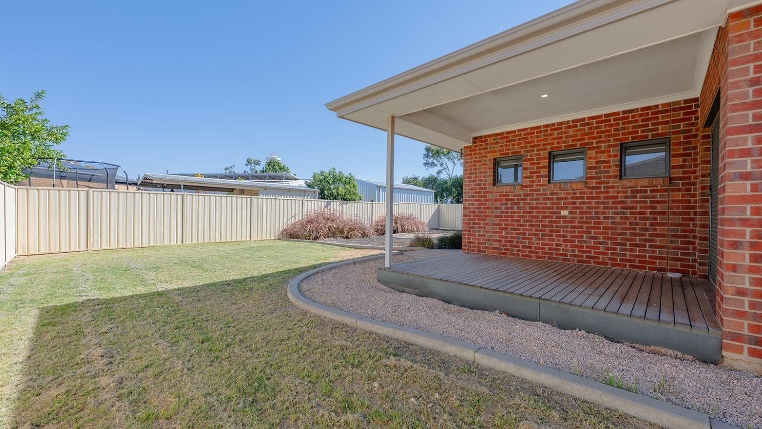 Backyard with wooden deck, brick house, and green lawn at La Trobe University Regional Housing – Mildura.