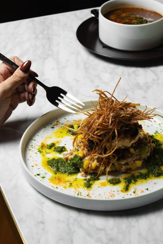 Hand with a fork reaching for grilled free-range chicken topped with crispy strands at Cypress & Oak Steakhouse, Frankfort