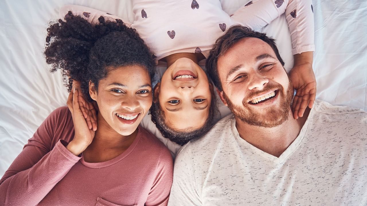 Mom, dad, and daughter laying on a hotel bed smiling