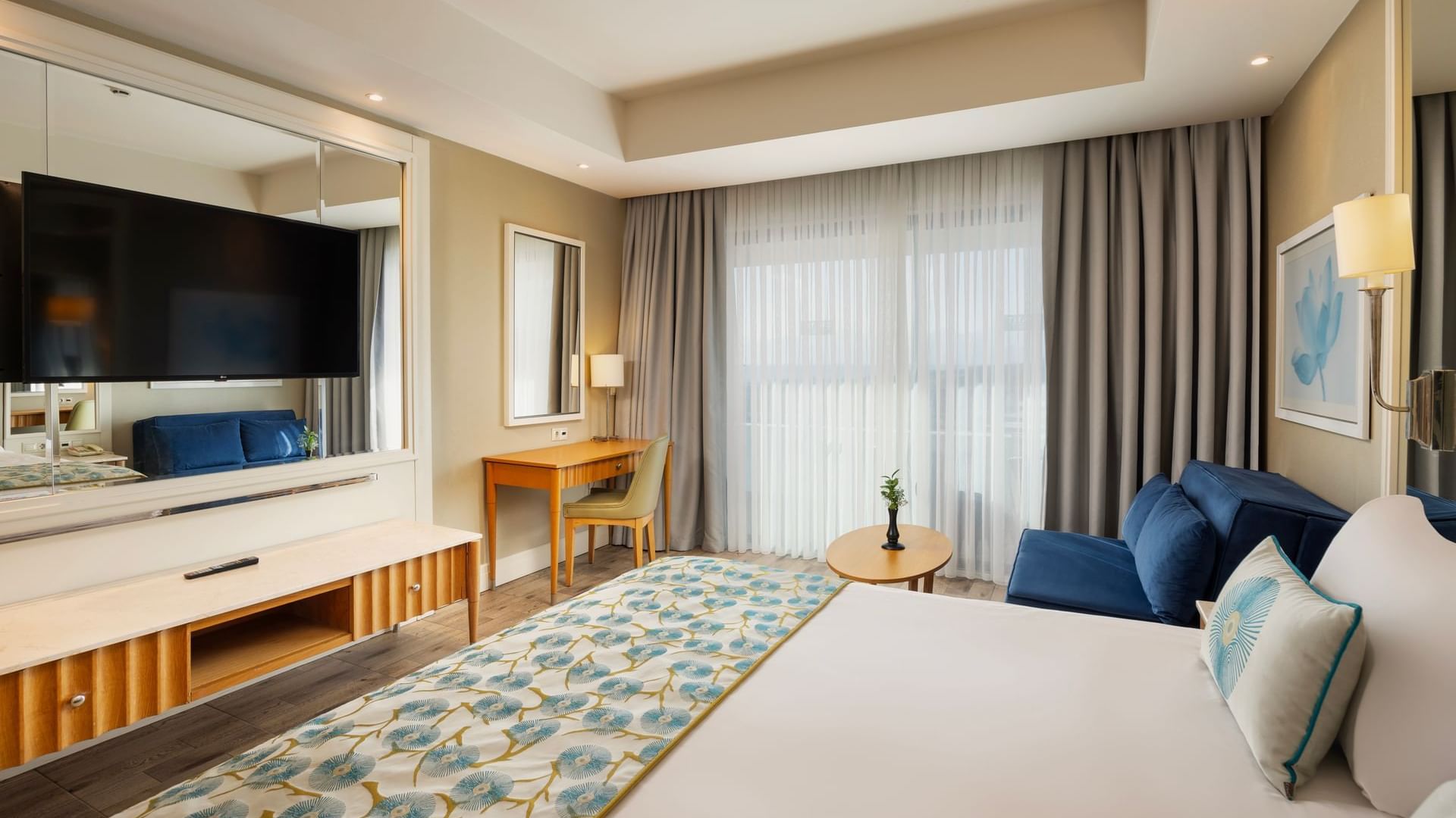Colonel Suite with a large bed featuring blue floral bedding, a blue sofa, a TV, and a desk at Titanic Deluxe Lara