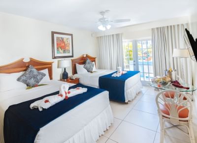Deluxe Room Double featuring two beds with decorative pillows, tropical decor, and a view of a pool at Bay Gardens Inn