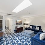 Spacious hotel suite with blue patterned carpet, navy sofas, skylight, and modern furnishings at el PRADO Hotel