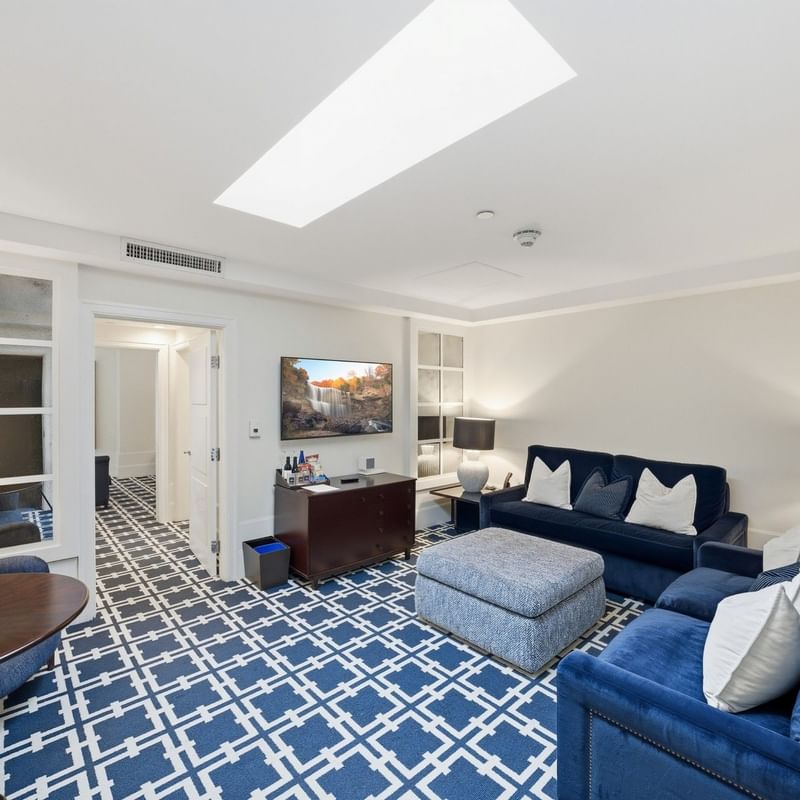 Spacious hotel suite with blue patterned carpet, navy sofas, skylight, and modern furnishings at el PRADO Hotel