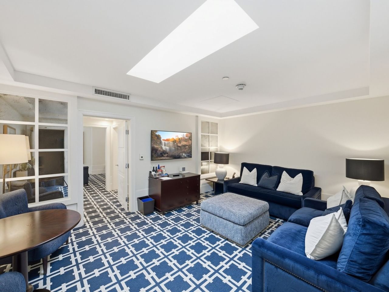 Spacious hotel suite with blue patterned carpet, navy sofas, skylight, and modern furnishings at el PRADO Hotel