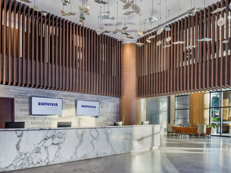Modern lobby reception desk with white marble finish, wooden wall slats, and creative hanging decor at Sunvivia Mazatlán
