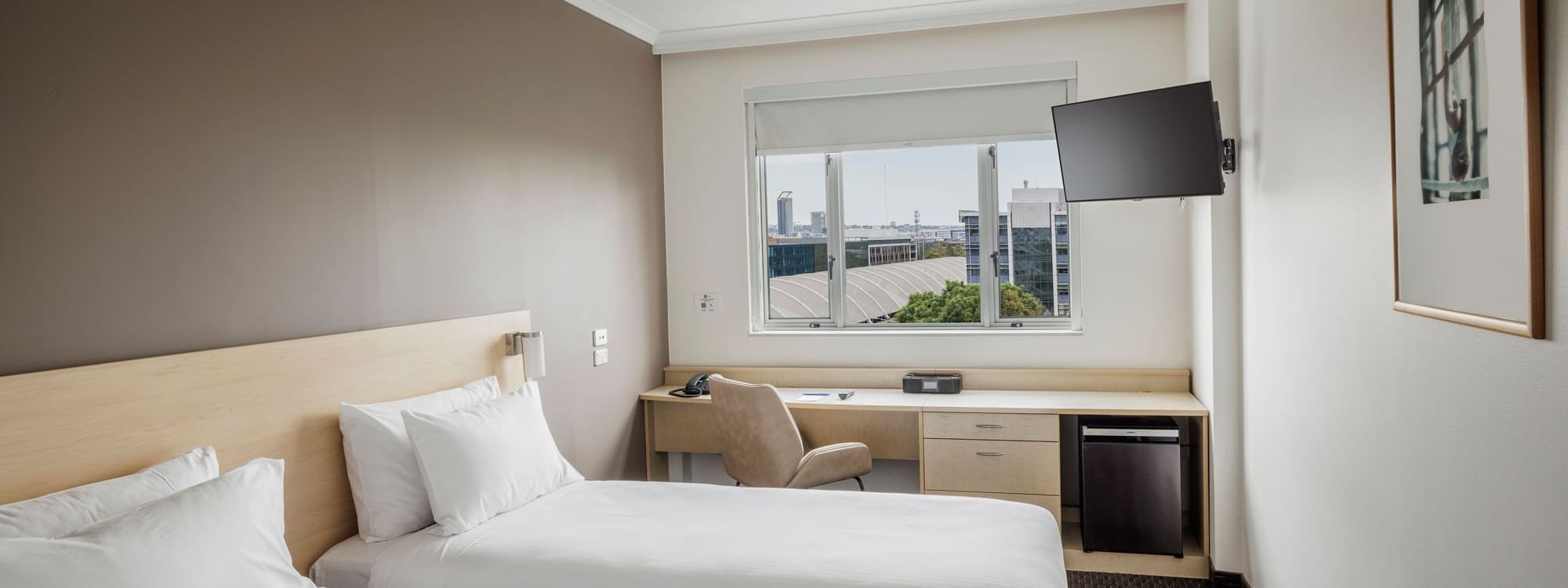 Wall-mounted TV & workspace by the beds in Standard Room 2 King Single Beds with a city view at Novotel Sydney Olympic Park
