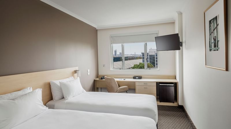 Wall-mounted TV and workspace by the beds in Standard Room 2 King Single Beds with a city view at Novotel Sydney Olympic Park