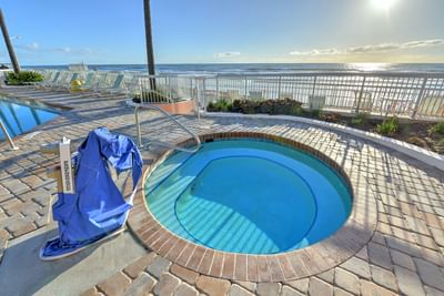 Daytona Bahama House outdoor hot tub with blue water, surrounded by brick, next to pool, with ocean view in background.