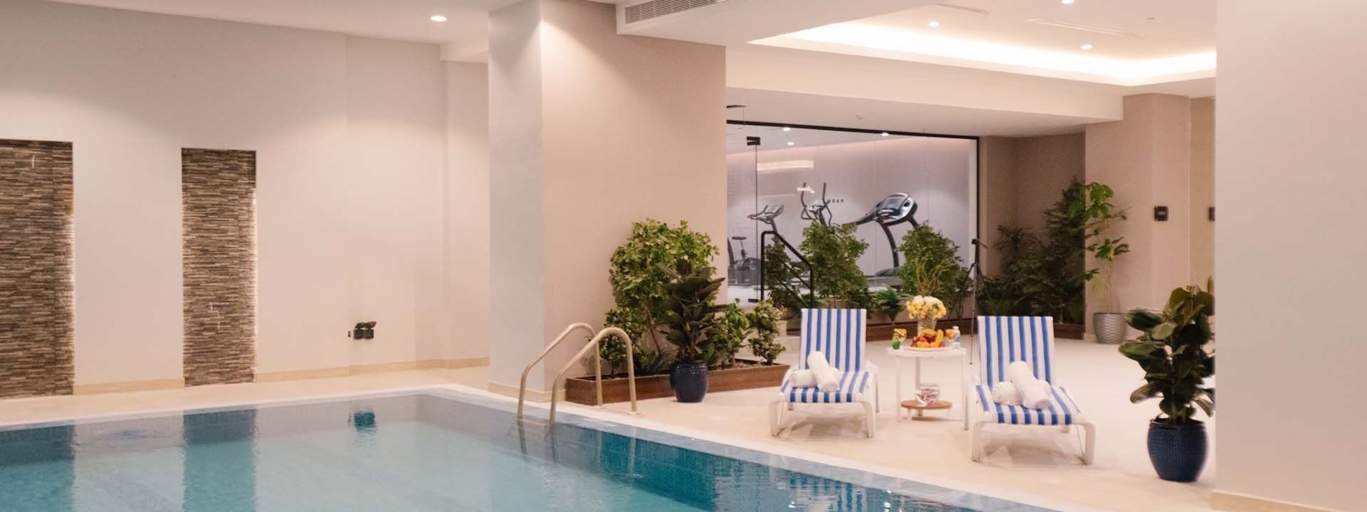 Indoor pool area with lounge chairs by a wall of plants under soft lights at Cantonal Hotel by Warwick Riyadh