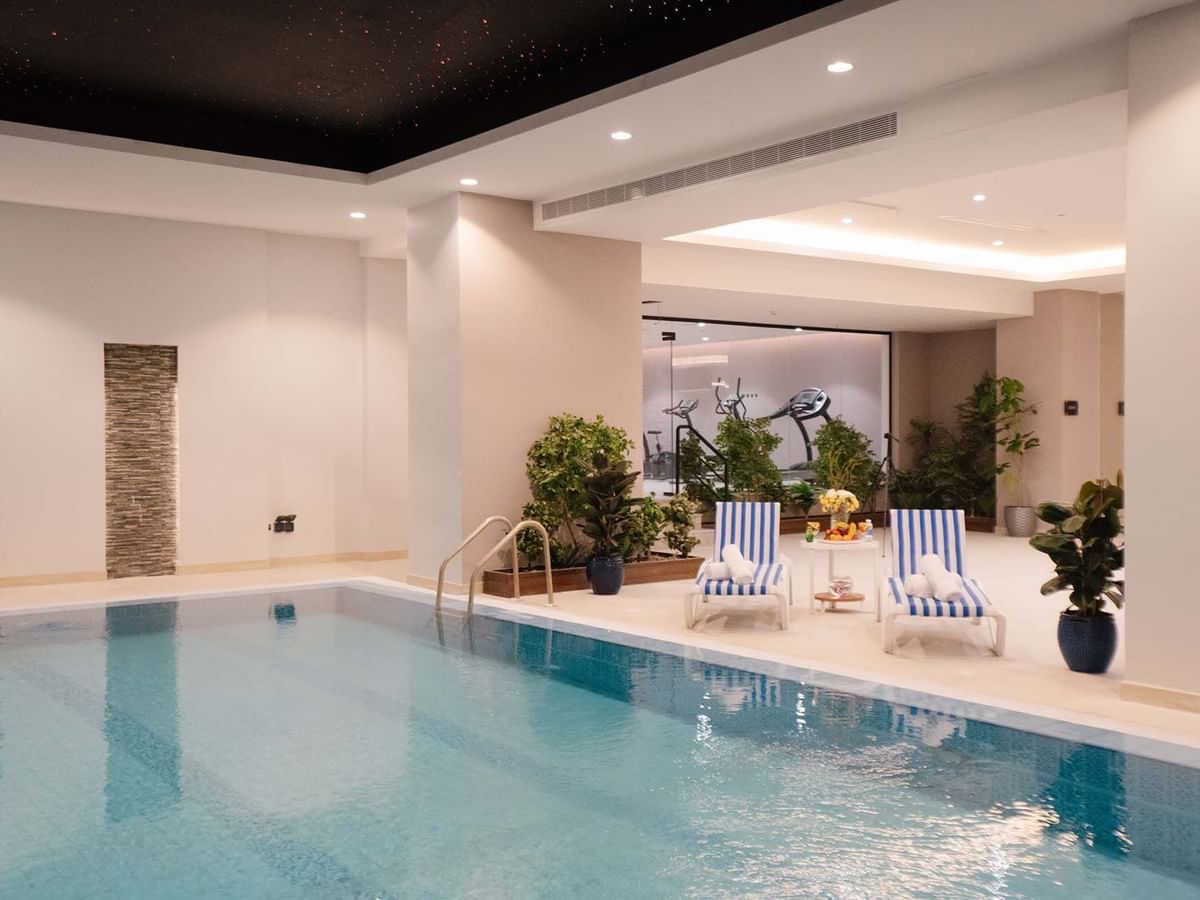 Indoor pool area with lounge chairs by a wall of plants under soft lights at Cantonal Hotel by Warwick Riyadh