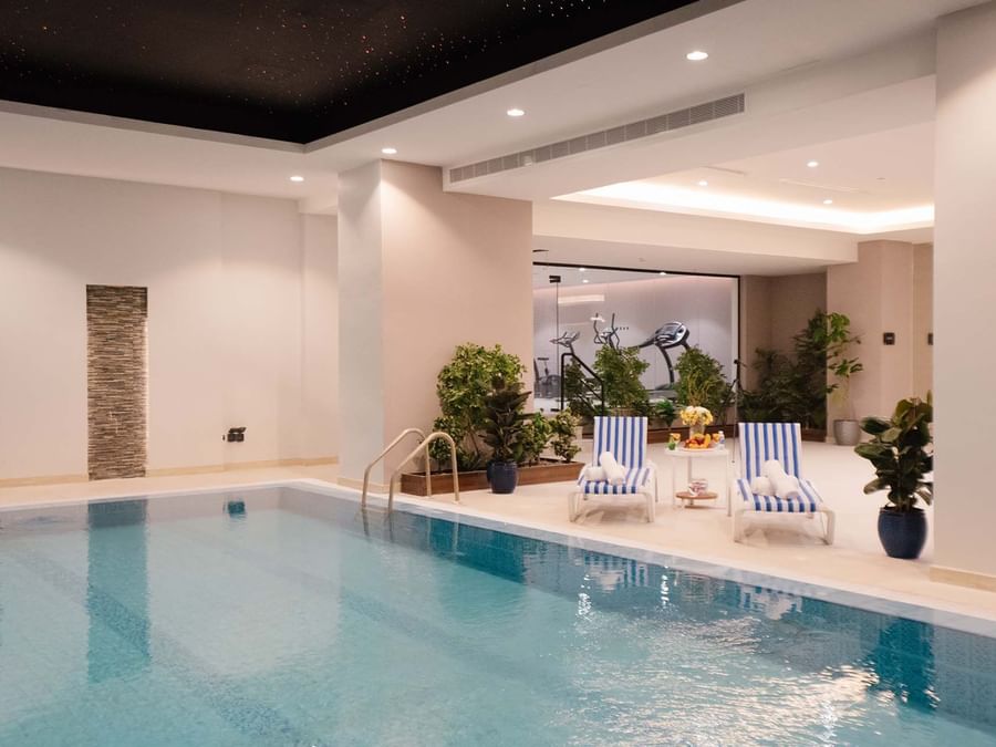 Indoor pool area with lounge chairs by a wall of plants under soft lights at Cantonal Hotel by Warwick Riyadh