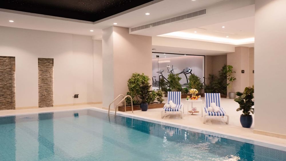 Indoor pool area with lounge chairs by a wall of plants under soft lights at Cantonal Hotel by Warwick Riyadh