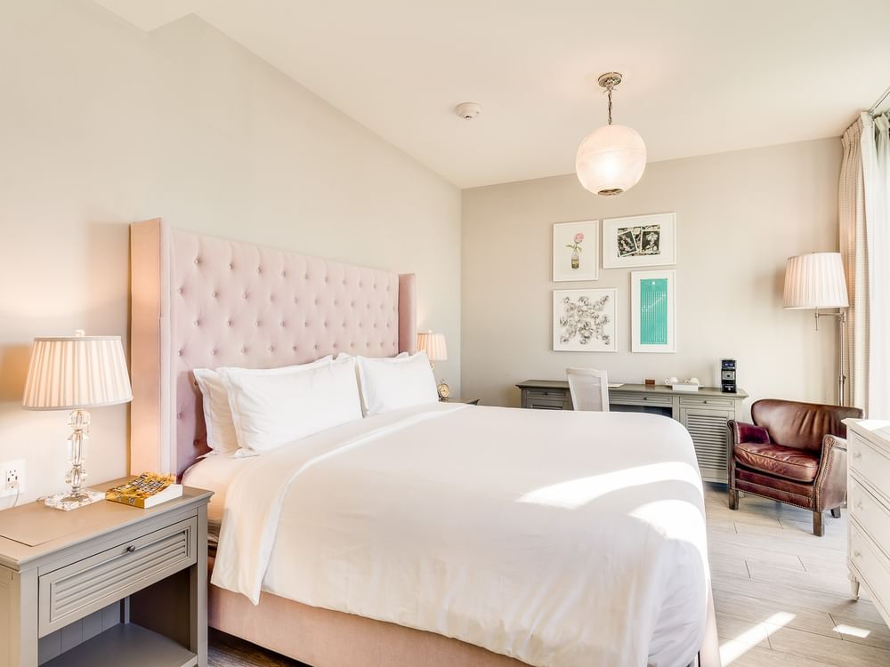 A wide view of a hotel room with a pink headboard, white bedding, and a desk.