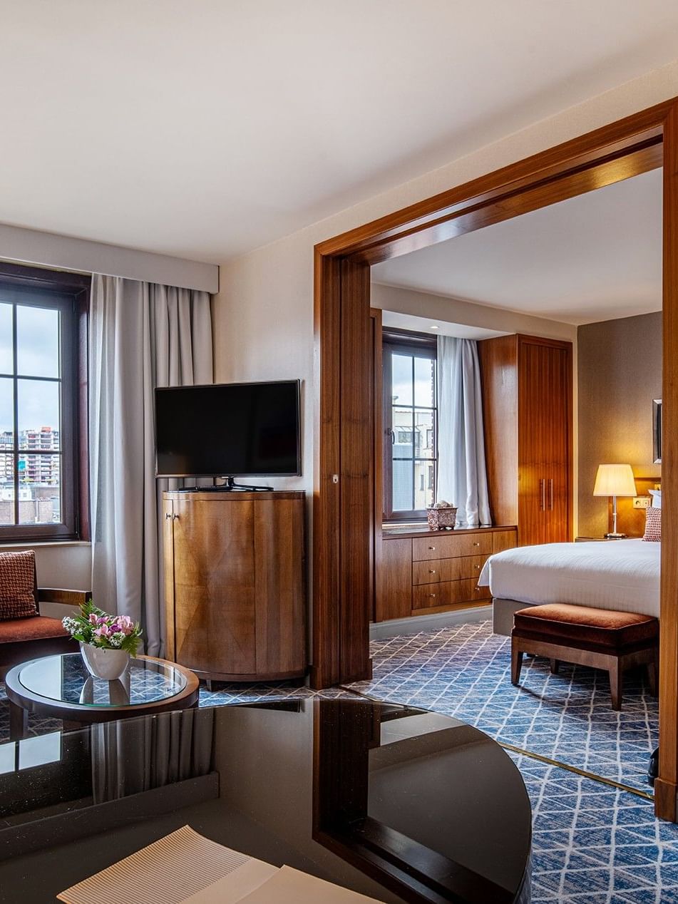 Elegant room with couch, TV, desk, and a bed in the background at Warwick Grand-Place Brussels.