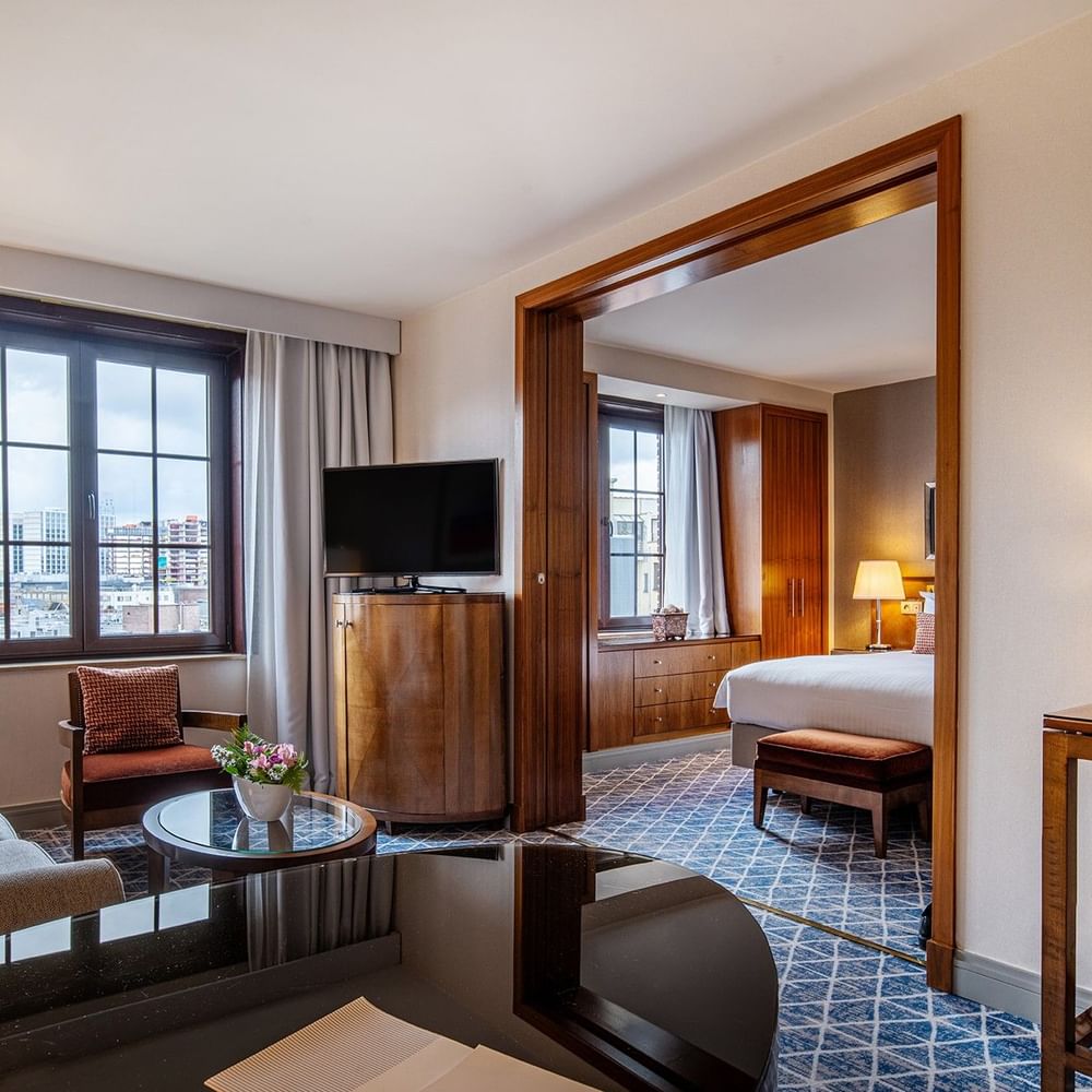 Elegant room with couch, TV, desk, and a bed in the background at Warwick Grand-Place Brussels.
