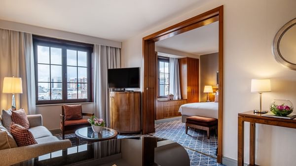 Elegant room with couch, TV, desk, and a bed in the background at Warwick Grand-Place Brussels.