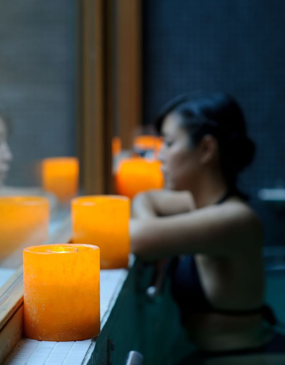 Velas laranja acesas na borda da piscina sob luz suave perto de hóspede relaxando no Noi Spa no NOI Vitacura