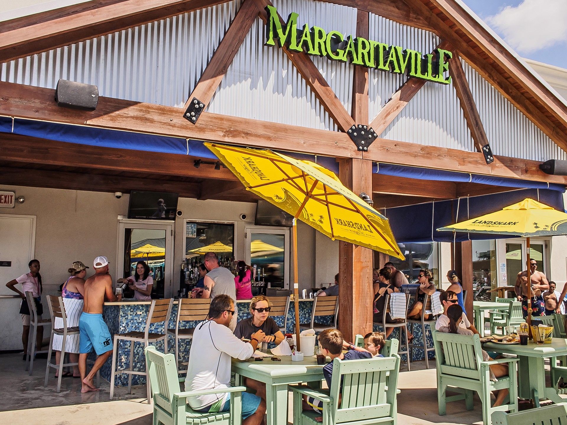 Guests enjoying outdoor dining and drinks in Margaritaville Café under yellow umbrellas at Margaritaville Resort Biloxi
