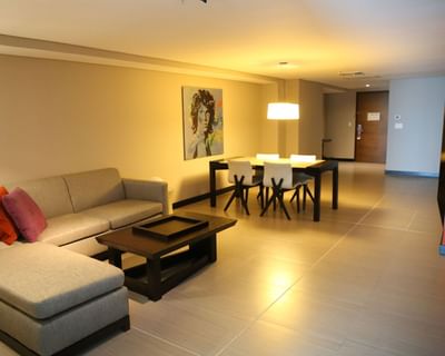 Sectional sofa and dining table under a pendant light near portrait art in the Presidential Suite at Megapolis Hotel
