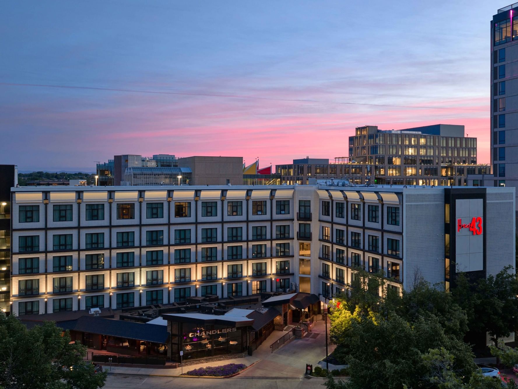 Modern hotel exterior illuminated at dusk with pink and blue sky and surrounding urban buildings