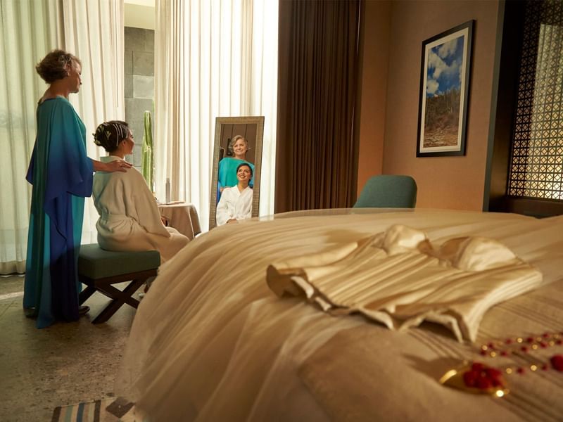 Bedroom interior with two individuals in robes and a dress lying on the bed at Grand Fiesta Americana