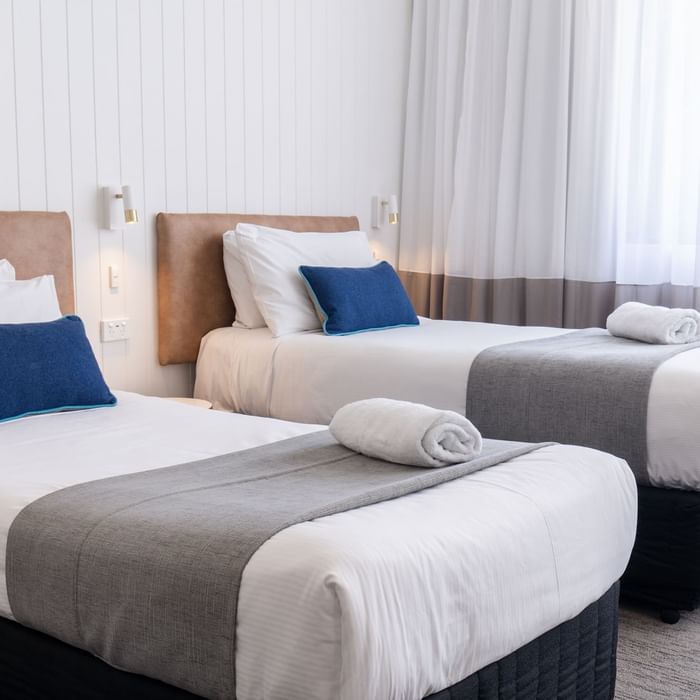 Two clean hotel beds with rolled towels on top at Mercure Charlestown.