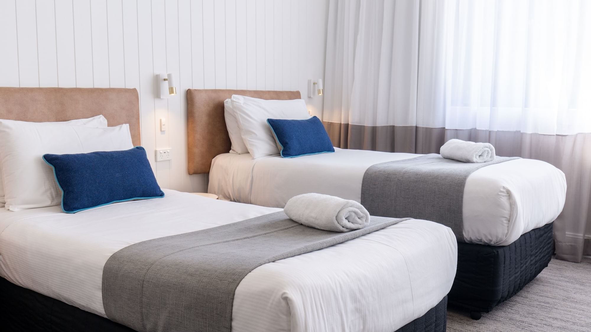 Two clean hotel beds with rolled towels on top at Mercure Charlestown.