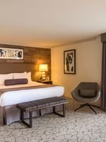 Plush king bed by a grey swivel chair under a wood wall with art in Accessible Deluxe Room at Warwick Denver
