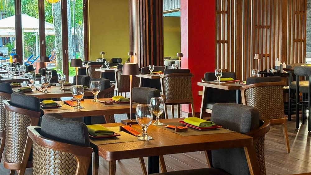Wood tables with woven chairs under floral ceiling art near a glass door in Sazanami at Warwick Fiji Resort and Spa