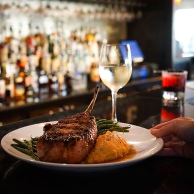 Gourmet grilled pork chop served with green beans and a glass of wine, served in Cora's Restaurant at The White House Hotel