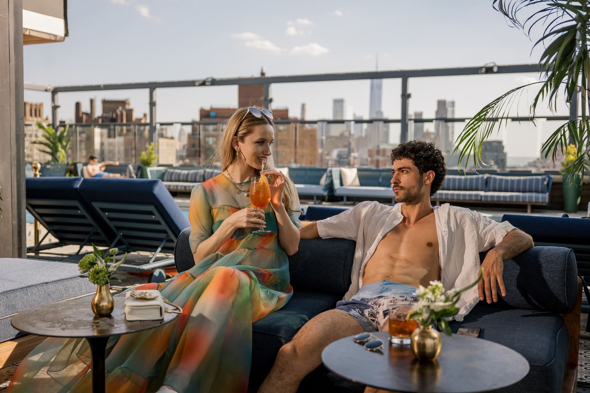 Couple toasting cocktails on rooftop lounge with blue seating and NYC skyline views at Gansevoort Meatpacking NYC