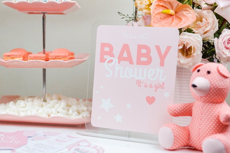 Pink-themed baby shower setup featuring a Baby Shower It's a girl sign, cupcakes, and a stuffed bear at Park Hyatt Saigon