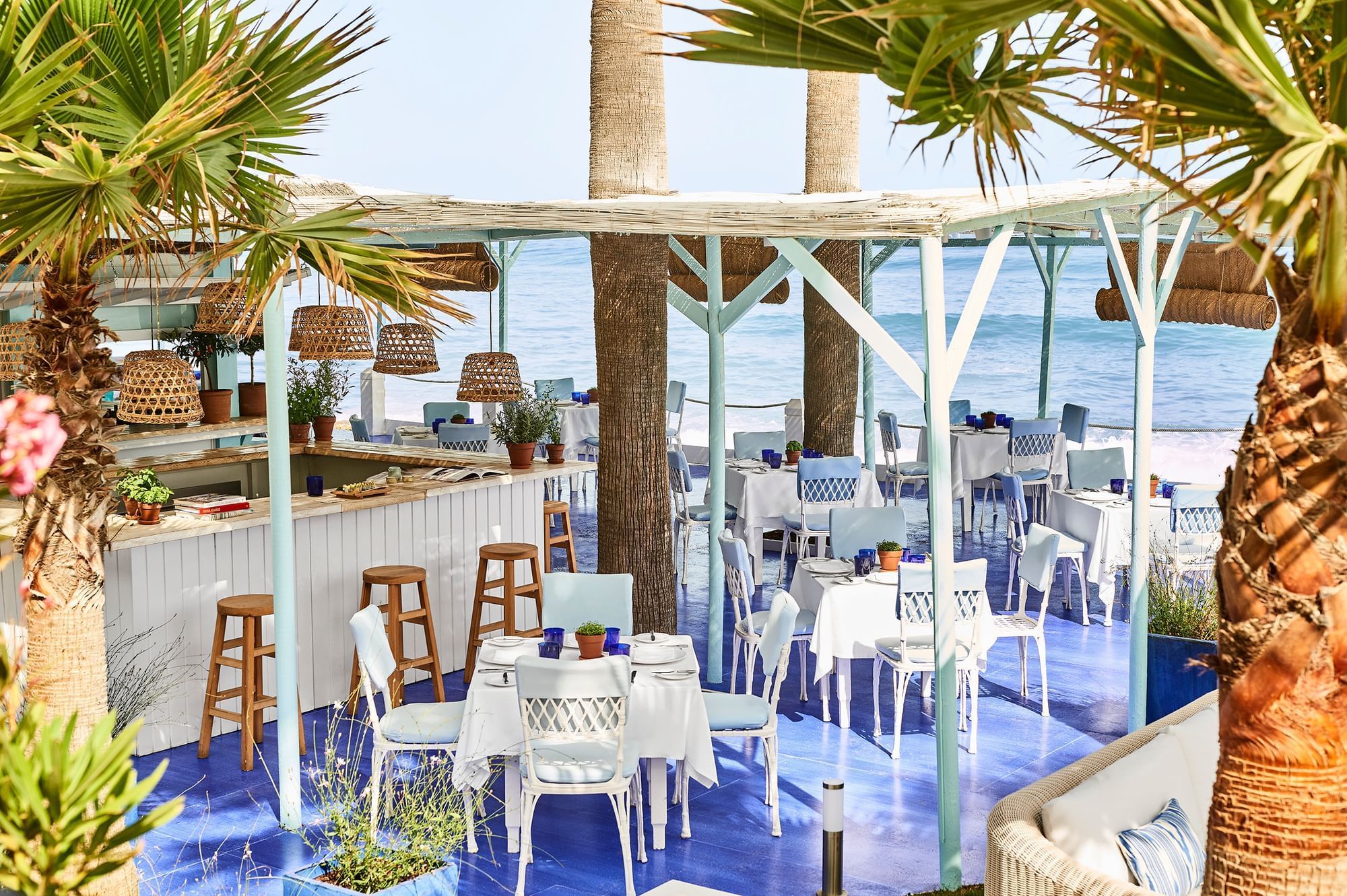 El Patio beachfront restaurant with stylish tables under a pergola and palm trees at Marbella Club by the sea